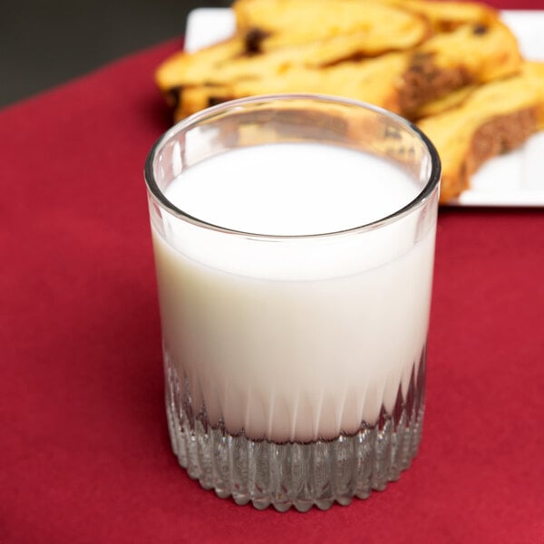 An Anchor Hocking Hampton rocks tumbler filled with milk on a red table.