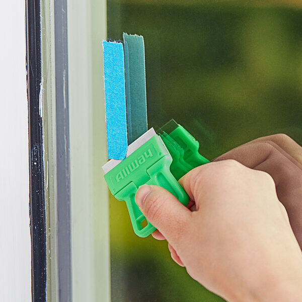 A person using a green Allway Tools mini glass scraper to clean a window.