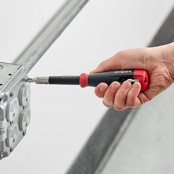 A person's hand using a red and black Allway Tools screwdriver to open a metal box.