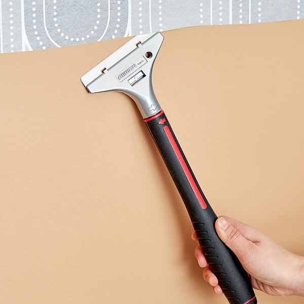A hand holding an Allway Tools aluminum-headed wall scraper with a black handle.