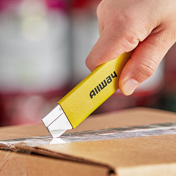 A hand holding a yellow Allway Tools Neon Easy Kutter cutting a box.