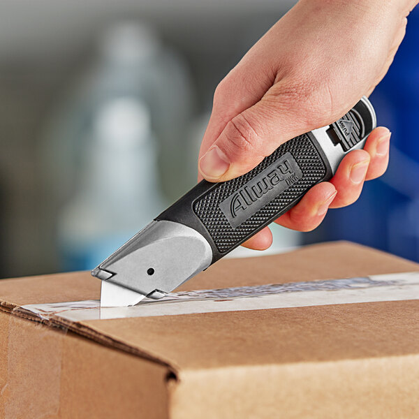 A hand holding an Allway Tools Soft-Grip Fixed-Blade Knife cutting a box.