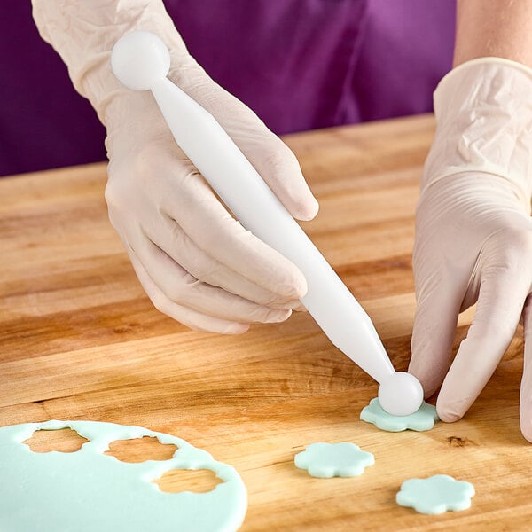 A person using Ateco double-ended ball tools to decorate a cake.