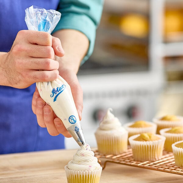 A person using an Ateco disposable pastry bag to frost a cupcake.