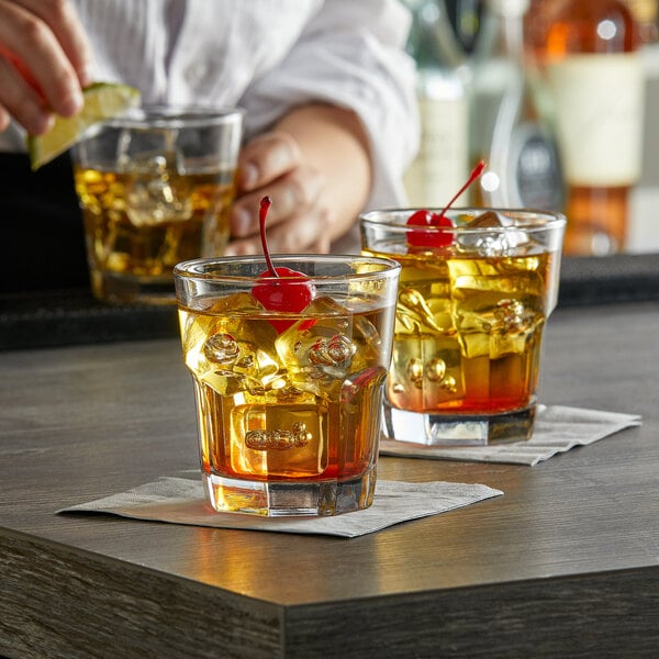 A bartender pours a liquid with ice into an Anchor Hocking New Orleans Rocks Glass with a cherry on top.