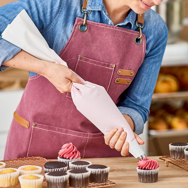 A person in a pink apron using an Ateco pastry bag to decorate a chocolate cupcake.
