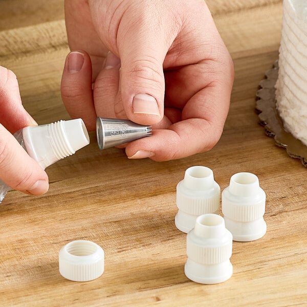 A person's hand holding a white plastic Ateco standard coupler.