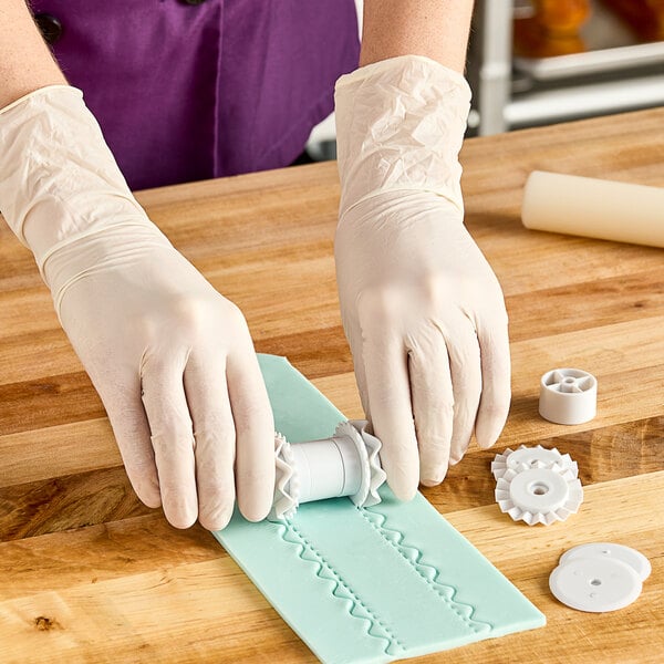 A person using an Ateco bow and ribbon cutter to make a pattern in dough.