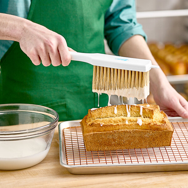 A person using an Ateco white pastry brush to brush a cake.