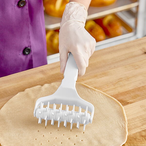 A person using an Ateco plastic dough docker to roll pizza dough.