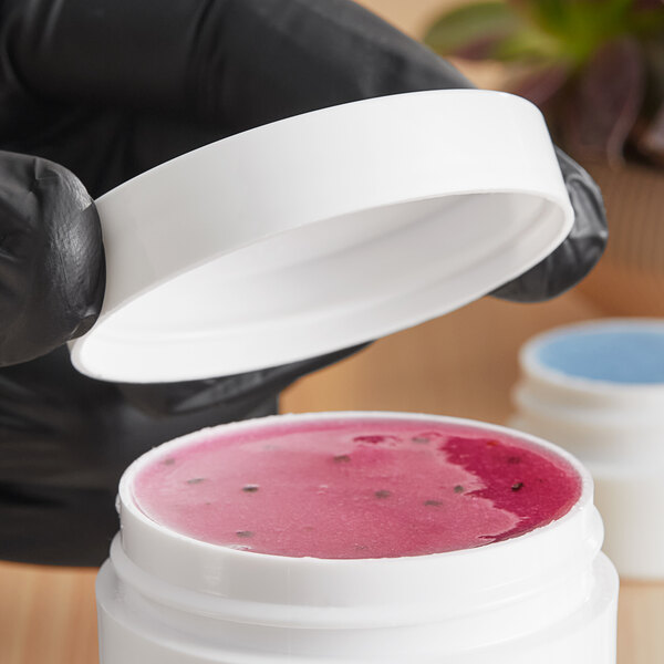 A hand in a black glove holding a white container of pink liquid with a 53/400 smooth unlined white lid.