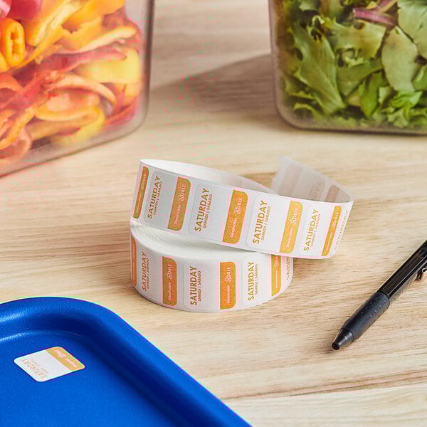 A roll of Noble Products Saturday Dissolvable Day of the Week labels next to a container of salad.