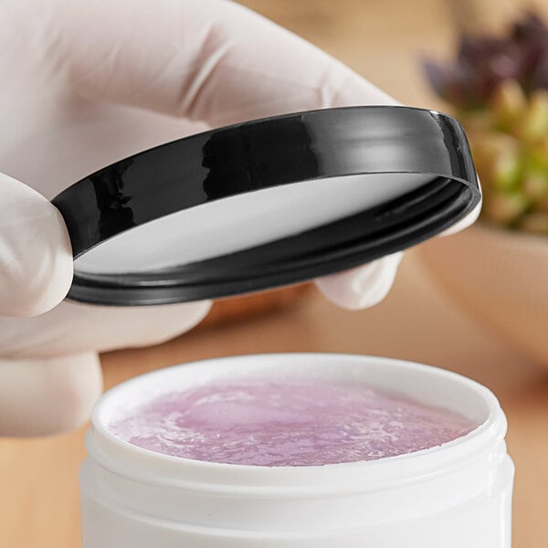 A hand holding a 70/400 smooth black lid over a white container with purple liquid.