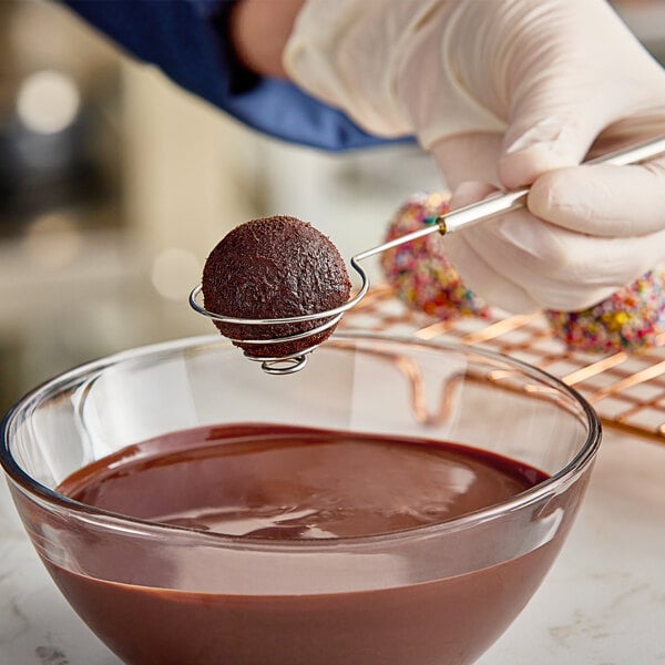 A person holding the Ateco stainless steel spiral dipping tool over a bowl of chocolate.