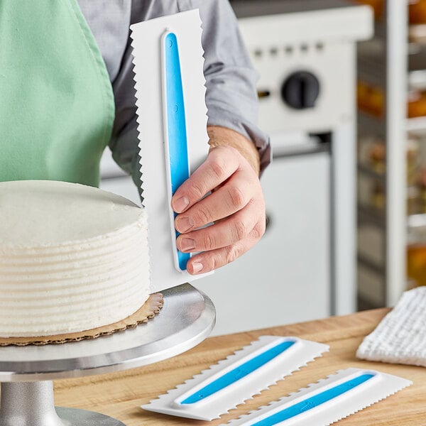 A hand using an Ateco plastic icing comb to cut a white cake.