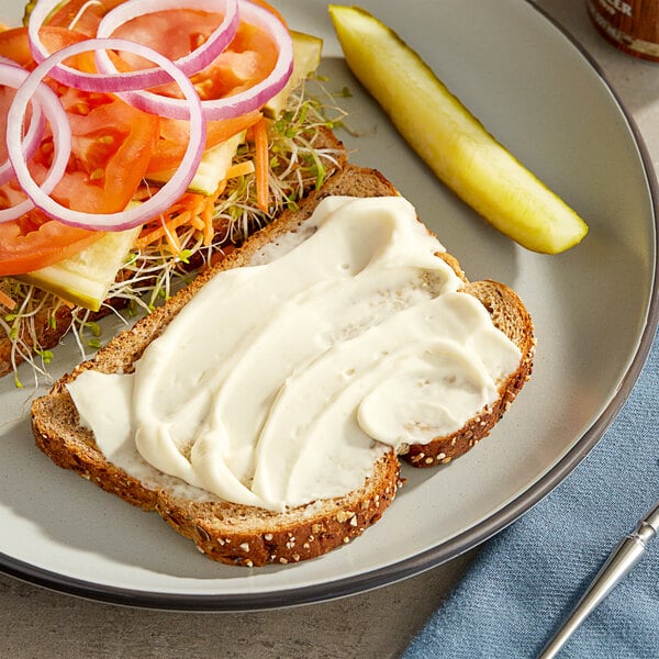 A plate with a sandwich and pickles with white spread on it.