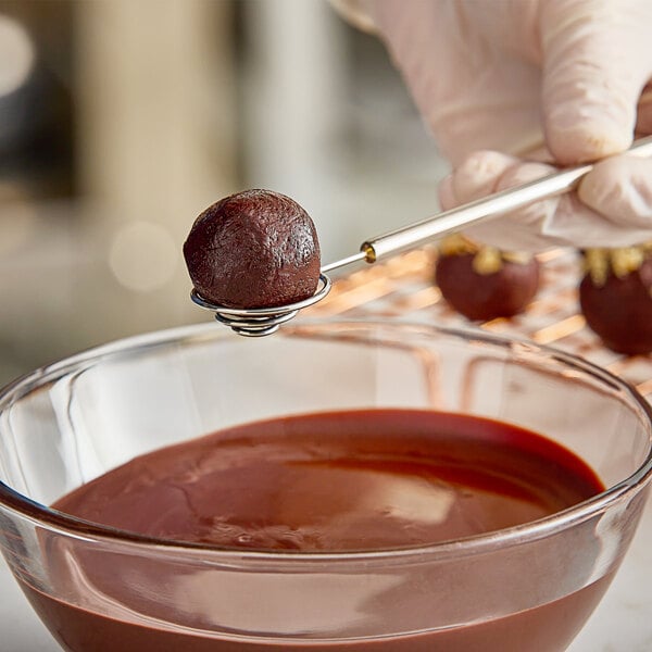 A person holding an Ateco stainless steel spiral dipping tool over a bowl of chocolate.