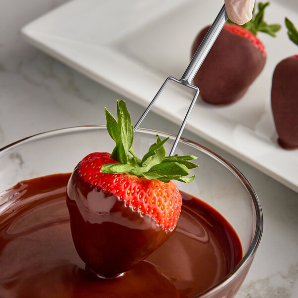 A strawberry being dipped in chocolate using an Ateco 2-Prong Dipping Fork.