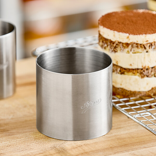 A round cake with a brown layer and a metal cylinder on a table.