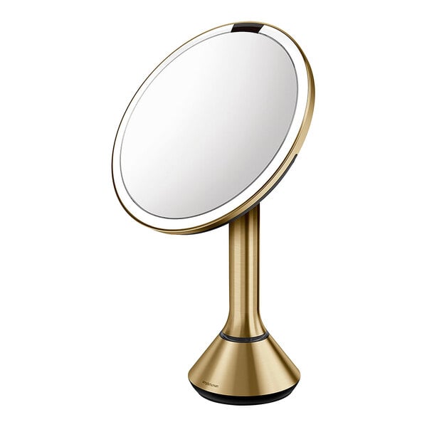 A simplehuman circular brass stainless steel sensor mirror on a gold stand.
