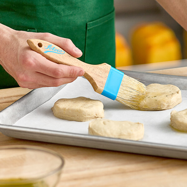 A person using an Ateco boar bristle baking brush with a wood handle to brush dough.