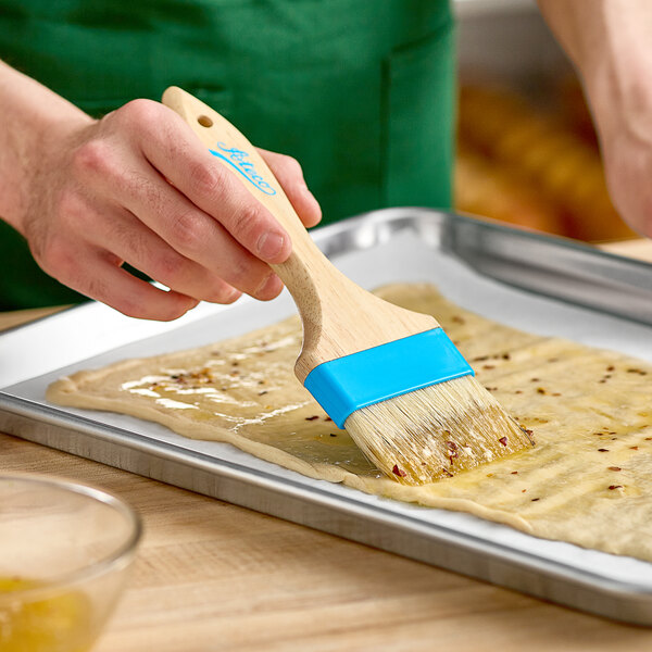 A person using an Ateco boar bristle pastry brush to spread dough on a baking sheet.