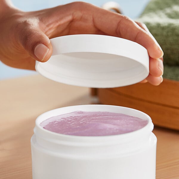 A hand holding a white plastic container of pink cream with a white 89/400 smooth unlined lid.