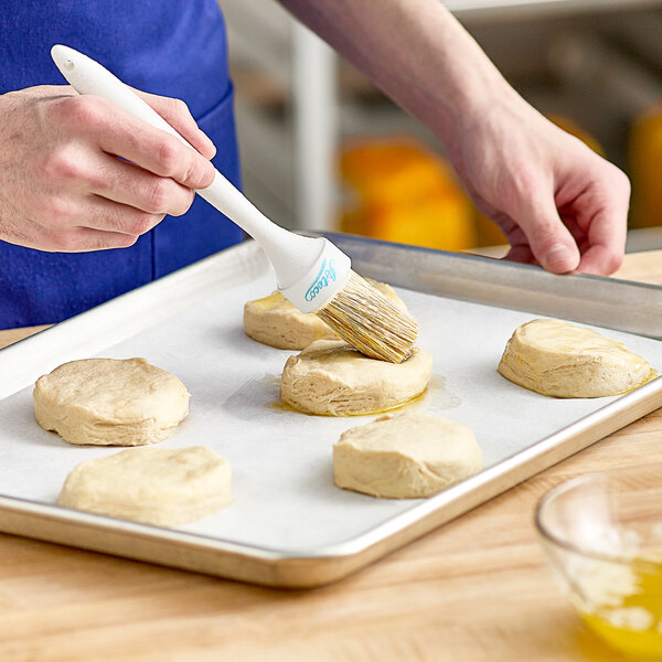 A person using an Ateco round boar bristle pastry brush to brush dough on a baking sheet.