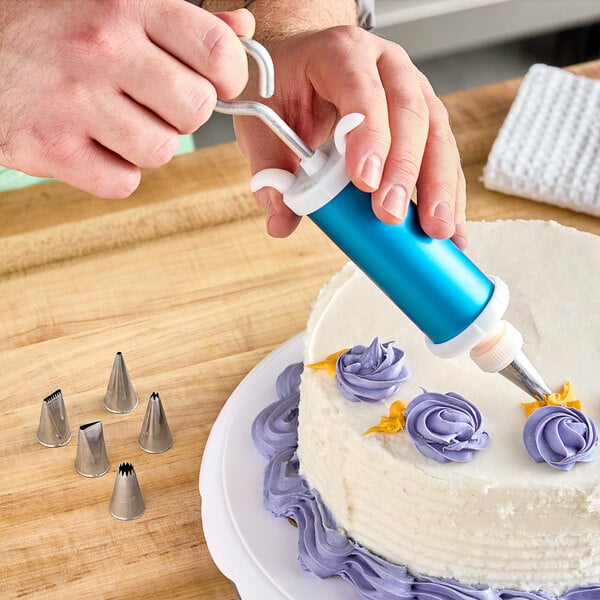 A person using an Ateco decorating syringe set to decorate a cake.