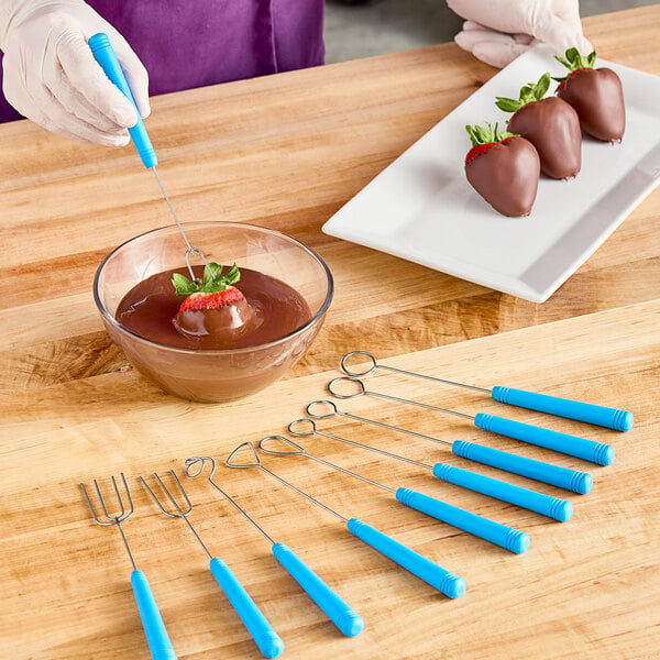 A person using an Ateco dipping tool to make a chocolate covered strawberry.