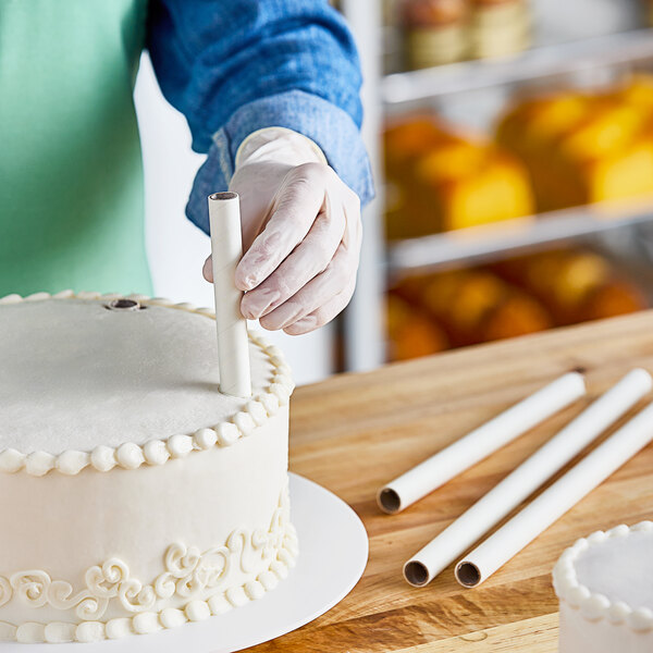 A person using an Ateco parchment-coated paperboard dowel to cut a cake.