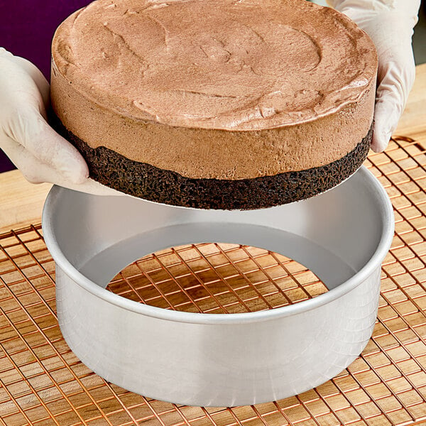 A person holding a chocolate cake made with an Ateco round aluminum cake pan with removable bottom.