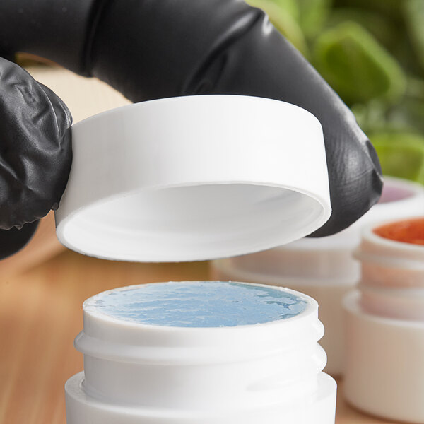 A person in black gloves holding a white container with blue and red paint.