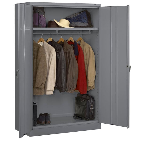 A dark gray metal Tennsco wardrobe cabinet with solid doors and clothes and bags inside.