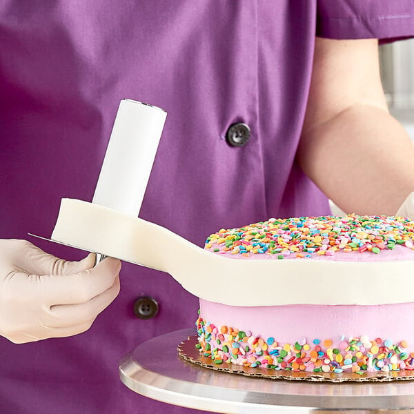 A person in purple scrubs using an Ateco stainless steel fondant strip applicator to cut a cake.