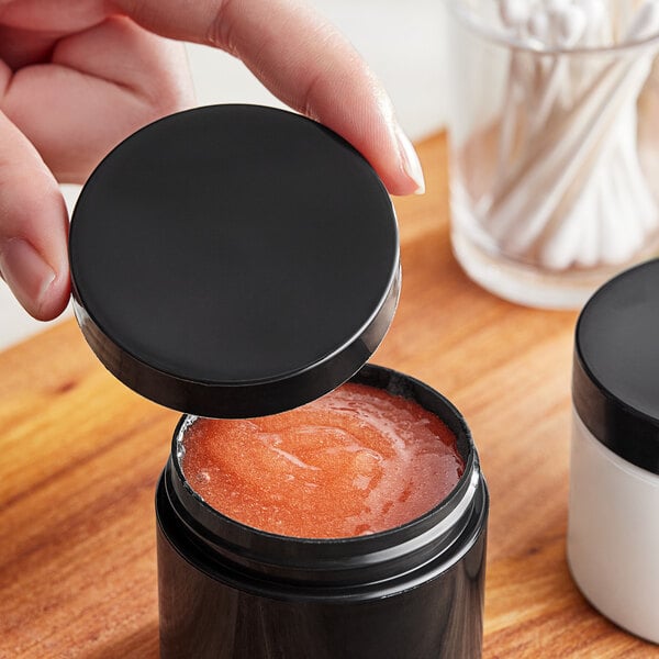 A hand holding a 58/400 smooth black lid over a container of pink liquid.