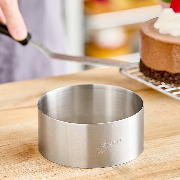 A round stainless steel cake mold on a wood surface.