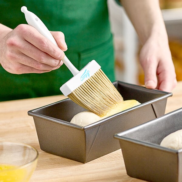 A person using an Ateco boar bristle brush to brush dough into a loaf pan.