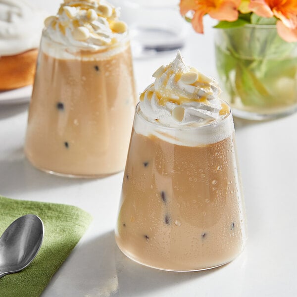 Two glasses of coffee with Guittard Sweet Ground White Satin Chocolate Flavoring Sauce, whipped cream, and chocolate chips.