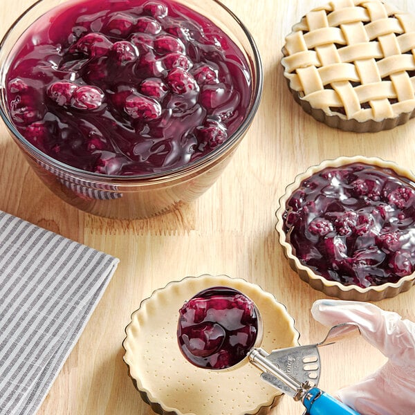 A hand using a spoon to add Lucky Leaf blackberry pie filling to a pie.