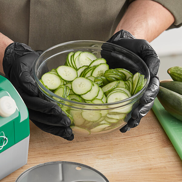 A person in black gloves uses an AvaMix 5/64" Slicing Disc to cut cucumbers on a counter.