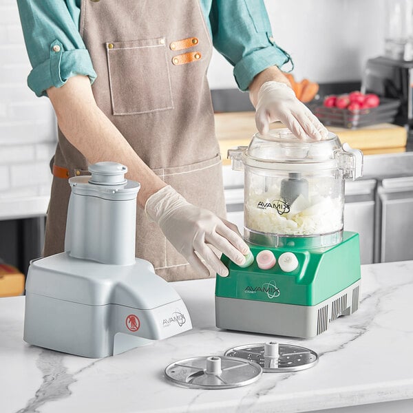 A woman in an apron using an AvaMix Cadet food processor on a counter in a professional kitchen.