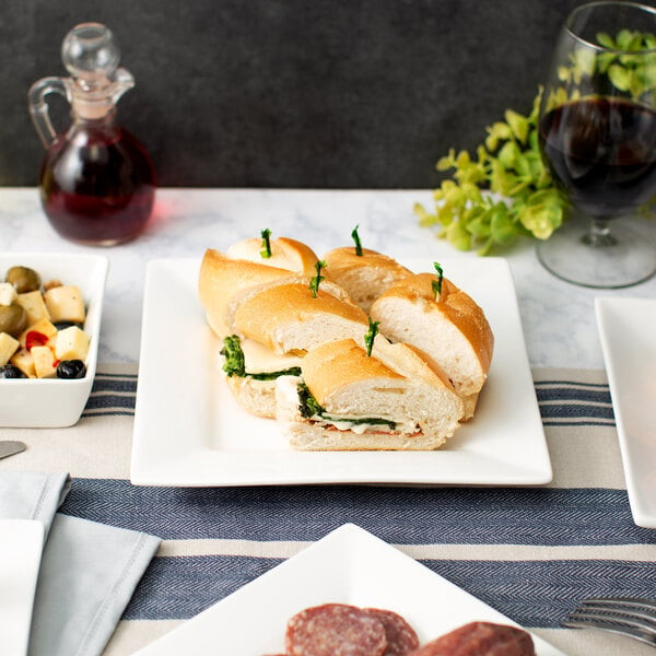 A 10 Strawberry Street white square porcelain luncheon plate with a sandwich on a table.