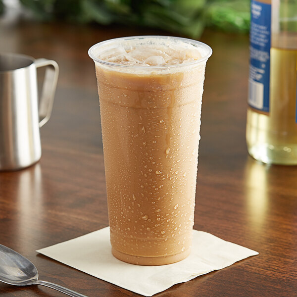 A clear plastic cup of brown liquid on a table with a spoon.