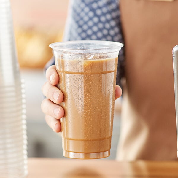 A hand holding a Choice clear plastic cup of brown liquid.