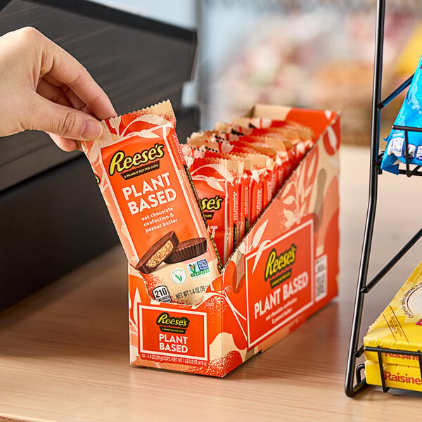 A hand holding a package of REESE'S Plant-Based Peanut Butter Cups.