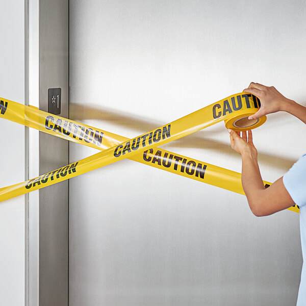 A woman's arm holding a yellow and black Xpose Safety "Caution" tape.