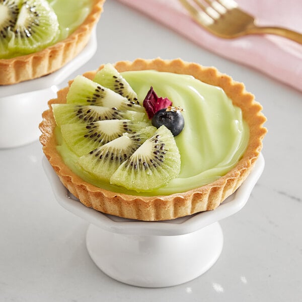 A fruit tart with kiwi on top on a white cake stand.