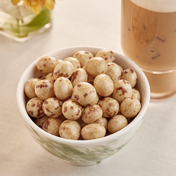 A bowl of Capora Marbled Chocolate Covered Espresso Beans next to a glass of coffee.