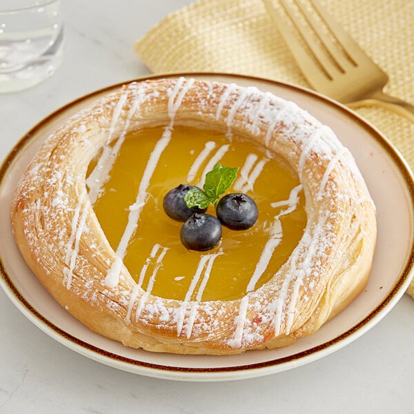 A pastry with blueberries and Perfect Puree Meyer Lemon Concentrate on a white plate with a fork.